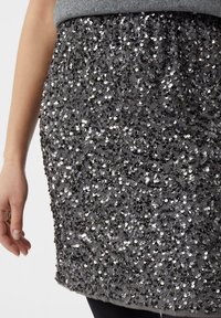 Czarna mini spódnica z cekinami z marszczonym pasem, pokryta gęsto okrągłymi cekinami, które odbijają światło, tworząc teksturowany wygląd.