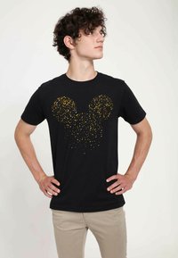 Černé tričko s krátkým rukávem s zlatým třpytivým siluetou Mickey Mouse vytvořenou z malých teček na přední straně. Měkká bavlněná tkanina.