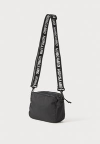 Black fabric crossbody bag with a rectangular shape, zippered top, and adjustable strap featuring white text "NØRGAARD."