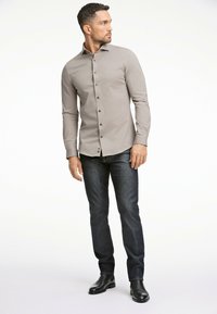 Camicia grigia con bottoni, maniche lunghe, design slim fit e jeans scuri. Tessuto liscio, bottoni marroni a contrasto e stile minimalista.