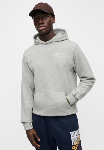 Γκρι βαμβακερό φούτερ με τσέπη μπροστά και κουκούλα με κορδόνι· διαθέτει μικρό λευκό λογότυπο στο αριστερό στήθος και ριμπ μανσέτες. Ναυτικό μπλε παντελόνι.