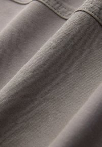 Grijze textiel met een glad, gestructureerd oppervlak, zichtbaar gemaakt met plooien en naden, die de stofsamenstelling en kleurvariatie benadrukt.