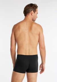 Boxer shorts en coton noir affichés de dos; présentent une coupe ajustée avec un design de ceinture simple et une texture lisse.