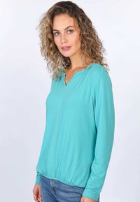 Türkiser Langarm-Top mit rundem Ausschnitt, an der Taille gerafft, aus weichem, leichtem Stoff mit glatter Textur.