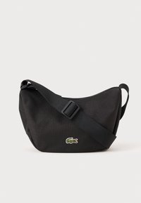 Black fabric shoulder bag with a curved shape, adjustable strap, and green embroidered crocodile logo. Durable material and smooth texture.