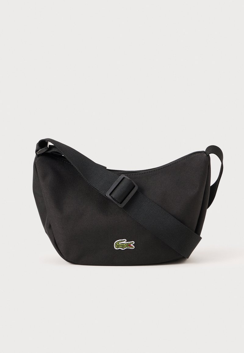 Black fabric shoulder bag with a curved shape, adjustable strap, and green embroidered crocodile logo. Durable material and smooth texture.