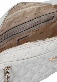 Gestikte witte handtas met zilveren hardware, voorzien van een ritssluiting, een patroonvoering met 'GUESS'-logo en een intern vak.