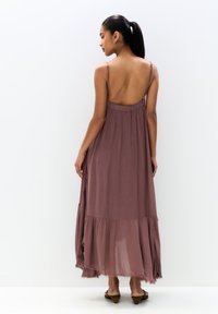 Robe longue couleur mauve en tissu léger avec des bretelles ajustables, un dos bas et un bas flottant, présentant un design à volants.
