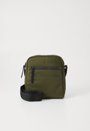 Sac bandoulière en tissu vert olive avec une poche zippée à l'avant, une sangle noire, un logo en relief et une forme rectangulaire. Matériau texturé et durable.