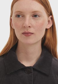 Schwarze Cordjacke mit breitem Kragen, Knopfverschluss und strukturiertem Stoff. Nahaufnahme, die das gesamte Design und die Details hervorhebt.