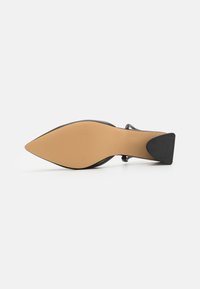 Black high-heeled shoe with a pointed toe, textured black upper, and a nude-colored sole featuring a slight heel and angular design.