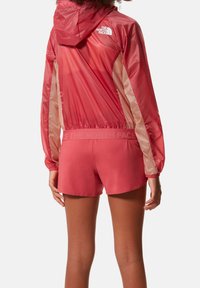 Röd lättviktsjacka och matchande shorts med en halvgenomskinlig design, elastisk midja och logodetaljer på båda plaggen.