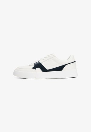 Hvit sneakers med marineblå semskede detaljer, med en glatt læroverdel, flate lisser og en tykk hvit gummisåle. Minimalistisk design.