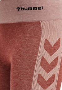 Legginsy w czerwono-różowe paski z szerokim pasem, teksturowanym materiałem oraz czarnym logo "hummel" wzdłuż górnej krawędzi i wzorzystym boku.