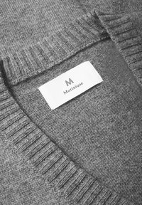 Detailný záber na šedý pletený golier svetra s bielou nálepkou, na ktorej je čierne logo "M" a názov značky "Martinique".