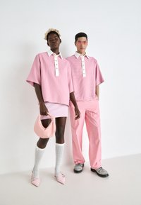 Két modell összehangolt, pasztell rózsaszín ruhát visel. A női modell laza, kockás felsőt, rövid szoknyát hord, és egy rózsaszín táskát visz magával. A férfi modell hasonló felsőt és rózsaszín csíkos nadrágot visel. Kiegészítők közé tartoznak a térd fölé érő zoknik és a hegyes orrú cipők.