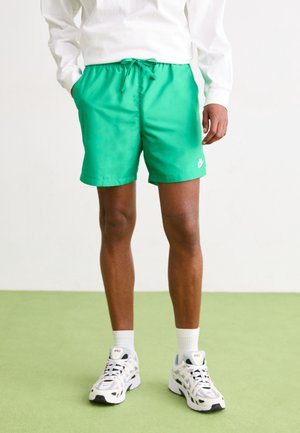 Grüne Sportshorts mit elastischem Bund und Kordelzug, seitlichen Taschen und weißem Nike-Logo am unteren Saum.