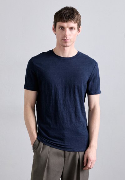 T-shirt bleu marine à manches courtes en texture douce avec un col rond. Porté avec un pantalon neutre, affichant une silhouette slim et ajustée.