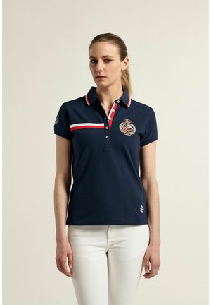 Polo navy con acentos a rayas rojas y blancas, de mangas cortas y emblema bordado en el pecho; fabricado en tejido de algodón texturizado.