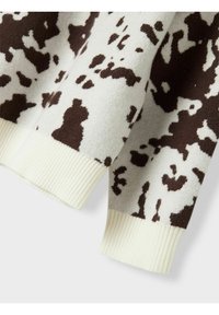 Maglione lavorato a maglia colore crema con motivi astratti marroni. Presenta polsini a costine in un solido colore crema chiaro, evidenziando una texture morbida.