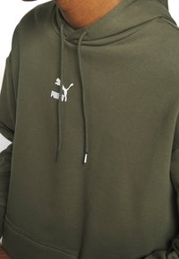 Sudadera con capucha verde oliva hecha de tela suave, con un bolsillo canguro, cordones ajustables y un logo blanco de Puma en el pecho.
