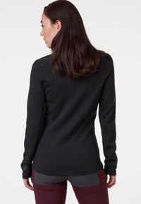 Zwart sportshirt met lange mouwen, een zachte textuur, een aansluitend ontwerp en accentstiksels. In combinatie met bordeauxrode leggings.