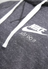 Grå bomullshuvtröja med kontrasterande vit dragsko och Nike-logotyp med texten "JUST DO IT" på framsidan. Texturerad tyg.