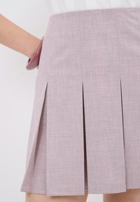 Falda plisada rosa claro hecha de tela texturizada, con una cintura ajustada y bolsillos laterales, diseñada para lograr una silueta estilizada.