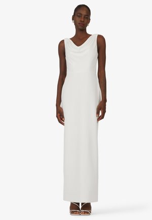 Long white dress featuring a cowl neck, sleeveless design, smooth texture, and a fitted silhouette, paired with strappy high-heeled sandals.