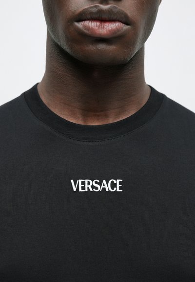 Μαύρο κοντομάνικο t-shirt με λευκό κεντημένο λογότυπο "VERSACE" στο στήθος και ραβδωτό ντεκολτέ. Λείος υφασμάτινος υφή.