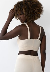 Beżowy prążkowany crop top z szerokimi ramiączkami i dopasowanym fasonem, o miękkiej teksturze i bezszwowych brzegach, w połączeniu z dopasowanymi prążkowanymi dolnymi częściami.