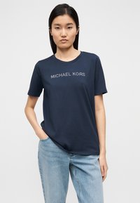 T-shirt de algodão azul-marinho com mangas curtas, decote redondo e logótipo "MICHAEL KORS" em detalhes metálicos no peito. Corte casual.
