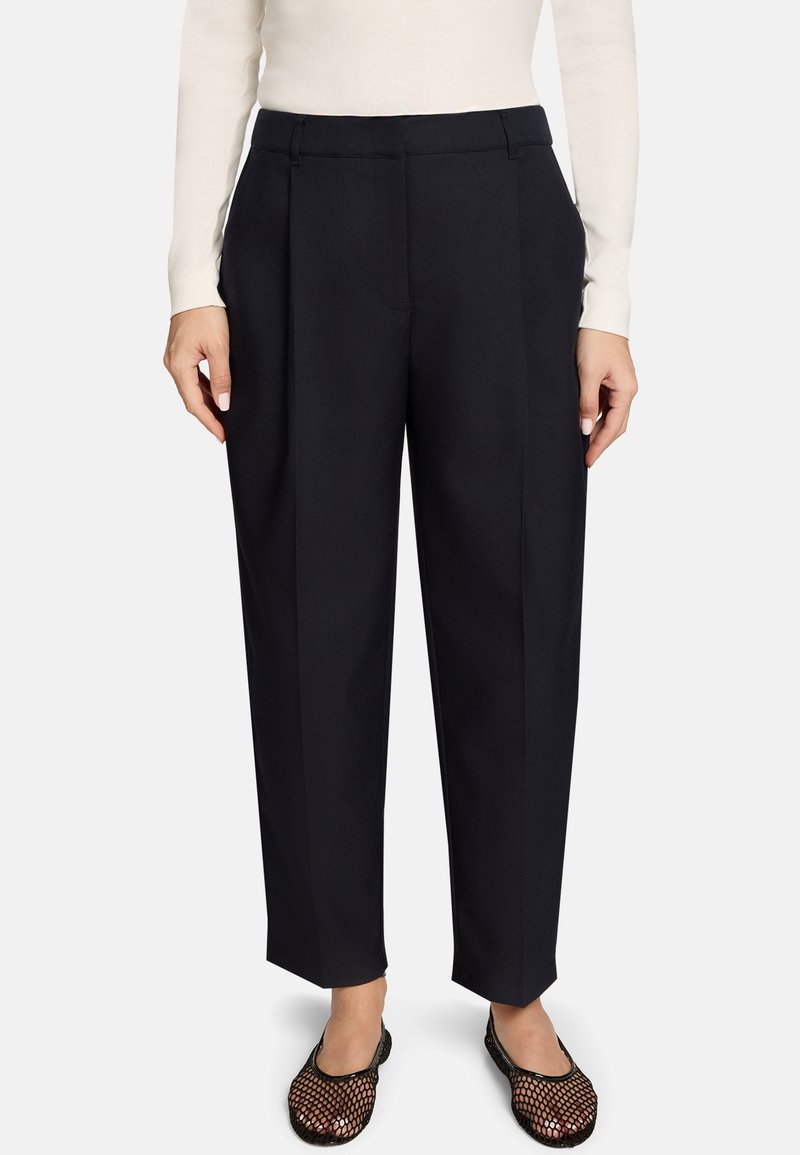 Pantalon noir à coupe cintrée, avec des plis, une texture lisse et un devant plat. Associé à des chaussures à enfiler en mesh.