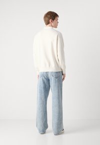 Λευκή μπλούζα με ριγέ στρίφωμα, συνδυασμένη με ανοιχτό μπλε παντελόνι σε ευρύ στυλ με δύο πίσω τσέπες και ξεθωριασμένη υφή.