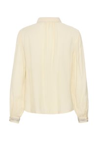 Blouse crème à manches longues avec tissu froncé au dos et aux poignets, avec poignets décoratifs boutonnés brodés en argent.