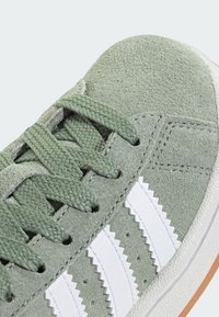 Zelené semišové tenisky s textúrovaným povrchom, s bielymi syntetickými pruhmi a zodpovedajúcimi šnúrkami. Gumená podrážka. Detailný pohľad.