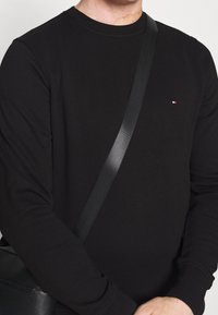 Felpa nera con scollo rotondo e maniche lunghe. Presenta un piccolo logo rosso e bianco sul petto. Tessuto opaco.