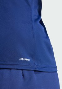 Top deportivo azul marino hecho de una tela suave y transpirable; presenta una textura sutil y el logo "AEROREADY" en la costura inferior.
