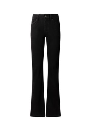 Femeie purtând o jachetă verde măsliniu cu nasturi, bluză albă, pantaloni negri cu curea și pantofi negri cu toc, stând în picioare pe un fundal simplu și deschis la culoare.