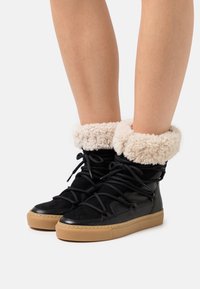 Czarne buty typu high-top wykonane z fakturowanej skóry, z puszystym kołnierzem w kolorze kremowym, czarnymi sznurówkami i jasnobrązową gumową podeszwą.