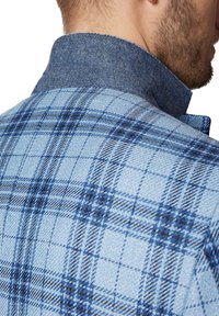 Niebieska koszula w kratę z teksturowanej tkaniny, z ciemnoniebieskim filcowym kołnierzykiem oraz skomplikowanymi wzorami w różnych odcieniach niebieskiego.