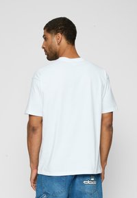 Hvid bomulds t-shirt med korte ærmer, rund hals og lige snit. Bemærkelsesværdig detalje inkluderer et lille logo trykt nær kanten.