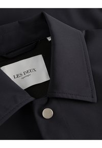 Dark navy collared shirt with a smooth fabric, featuring a silver snap button and a white label reading "LES DEUX copenhague."