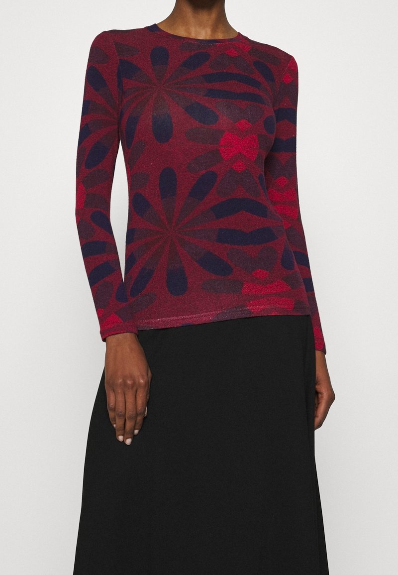 Dlouhý rukáv přiléhavý top s velkými abstraktními květinovými vzory v červené a tmavě fialové barvě, spárovaný s jednoduchou černou sukní.
