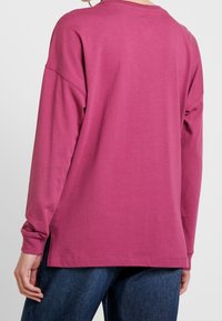 Langarmshirt in Fuchsia, aus weichem Baumwollstoff, mit seitlichen Schlitzen, überschnittenen Schultern und einem geraden Saum mit einfachen Nähten.