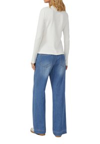 Weißes, geripptes Langarmshirt mit rundem Ausschnitt, kombiniert mit weiten blauen Jeans mit Gesäßtaschen und glatter Textur.