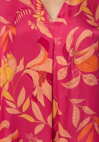 Tela fucsia con grandes patrones florales y de hojas en tonos naranjas y amarillos, con un diseño de cuello en V y textura suave.