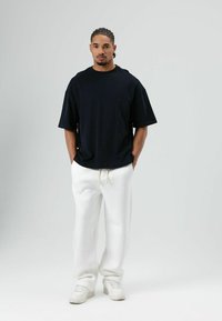 Zwart oversized T-shirt van katoen, gecombineerd met witte joggingbroek in een zachte textuur en crèmekleurige sneakers. Eenvoudig, casual ontwerp.