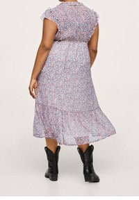 Kukallinen midi-mekko, jossa on lyhyet röyhelöhiha, pastellivärinen vaaleanpunainen ja sininen kuosi, kapeat vyötärö ja kerroksellinen helma; käytetty mustien nilkkureiden kanssa.