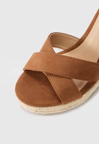 Sandalo wedge in suede marrone con fasce incrociate, punta tonda e suola in juta intrecciata naturale. Fodera interna liscia per il comfort.